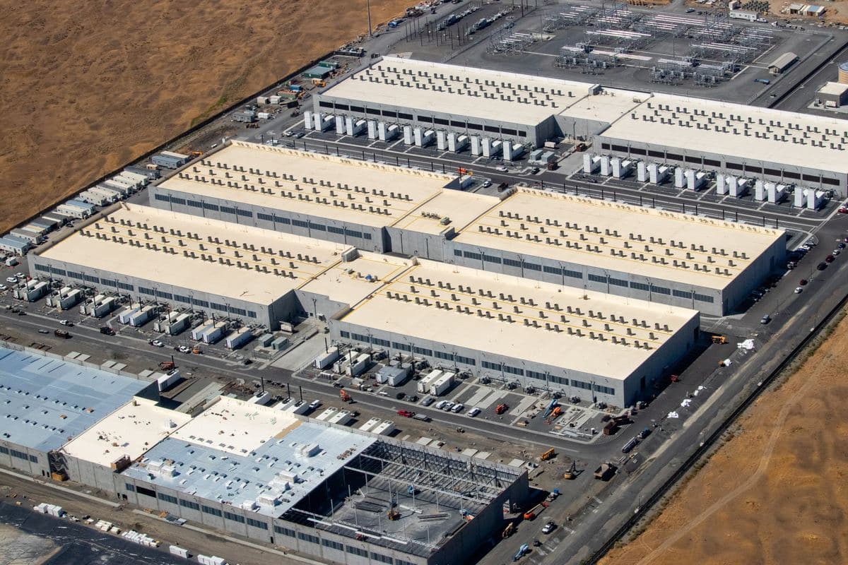 Aerial view of a large data center campus with rows of server buildings and nearby electrical substation