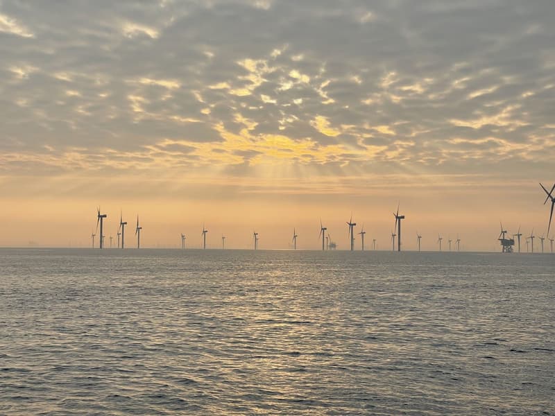 Offshore wind turbines silhouetted against a golden sunset sky over the sea