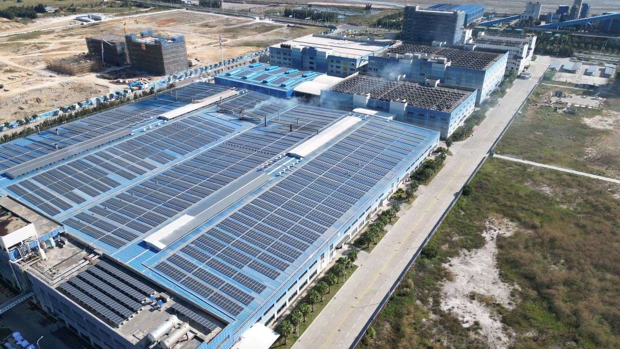 Aerial view of a large industrial complex with solar panels covering its rooftops