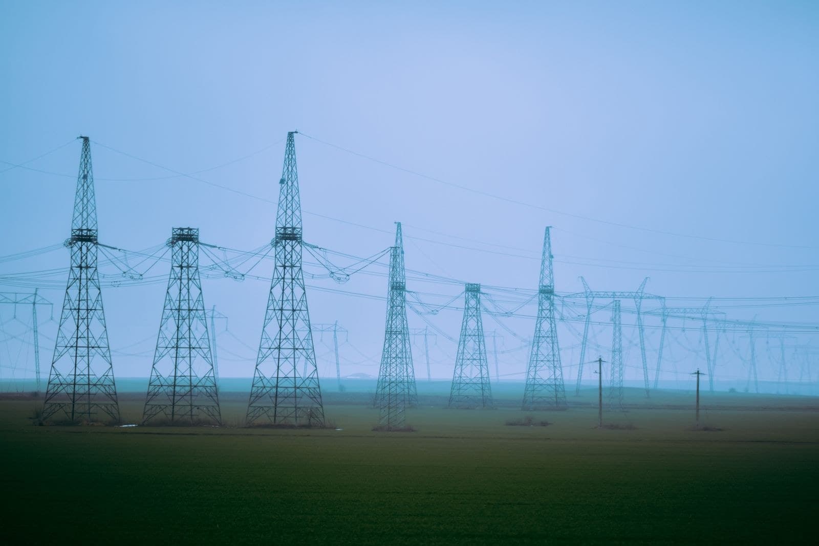 High-voltage transmission towers crossing a rural field under a blue sky