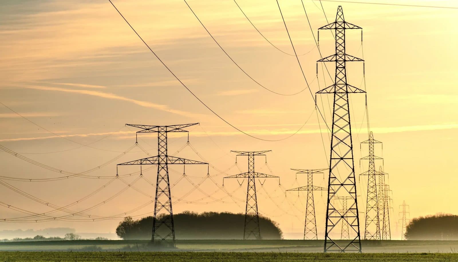High-voltage transmission towers and power lines under a hazy late-afternoon sky
