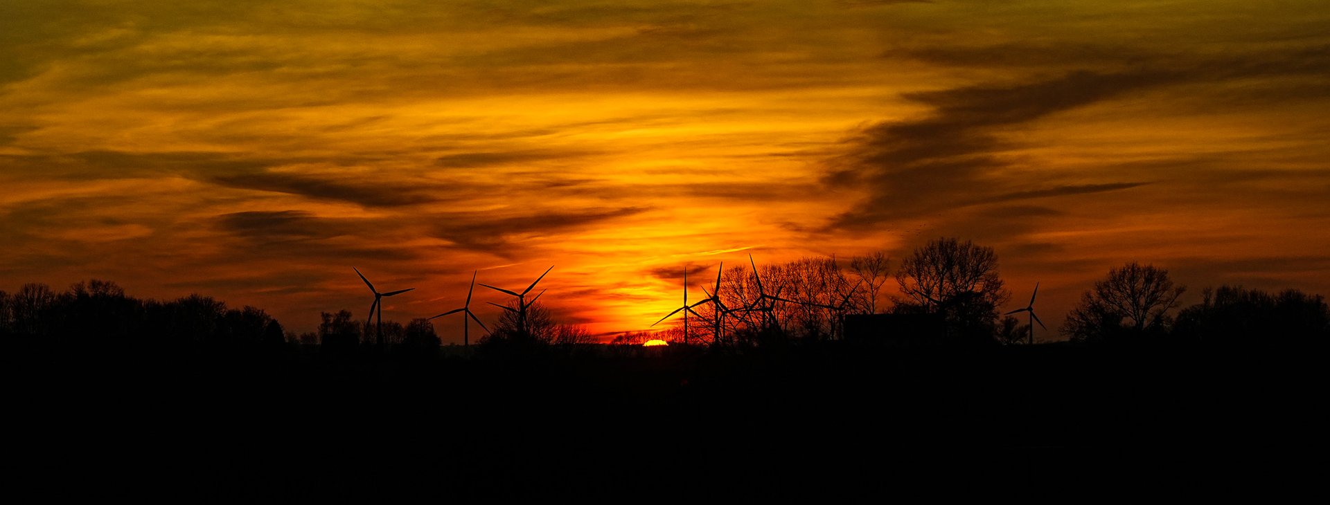Wind turbines silhouetted against a sunset sky (illustrative photo)